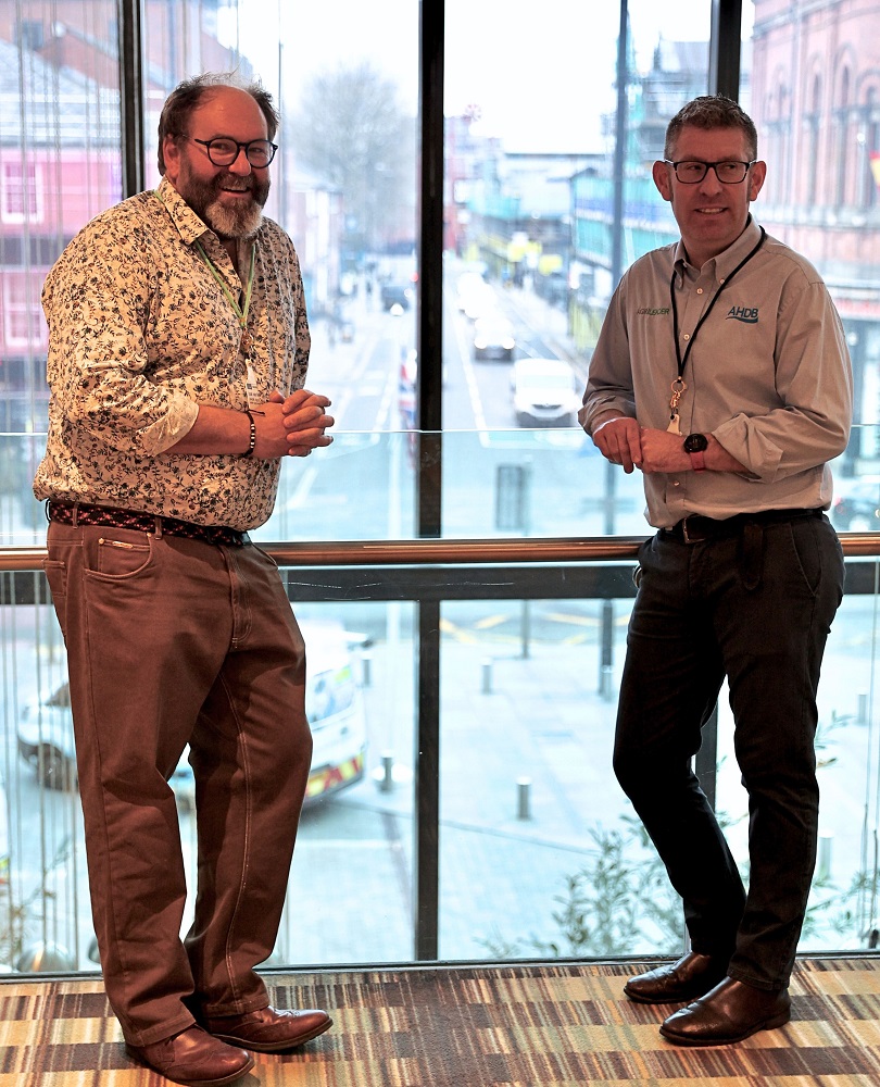 Two men (Izak and Mark) stood leaning against an indoor balcony in front of a large window